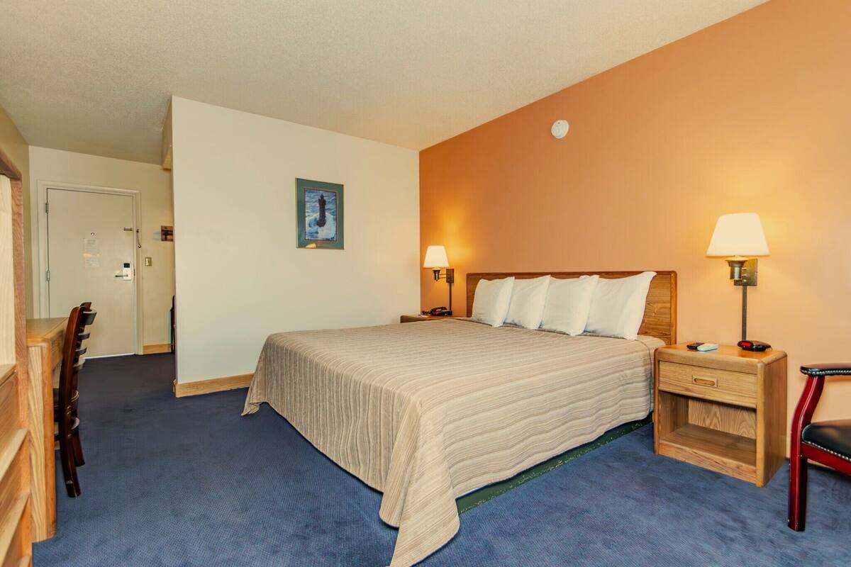A hotel room with a large bed, two bedside tables with lamps, a wooden chair, and a desk with a chair.