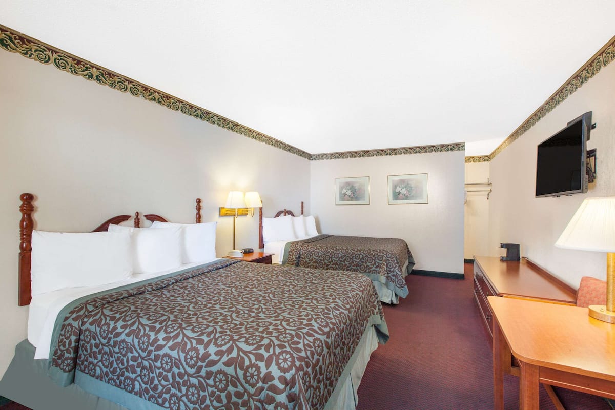 Quarto de hotel com duas camas, uma escrivaninha, uma cadeira, uma televisão e duas quadros na parede.