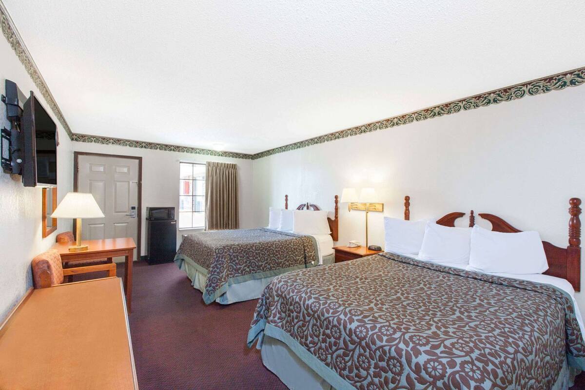 Quarto de hotel com duas camas, uma escrivaninha, uma televisão e uma janela com cortinas.