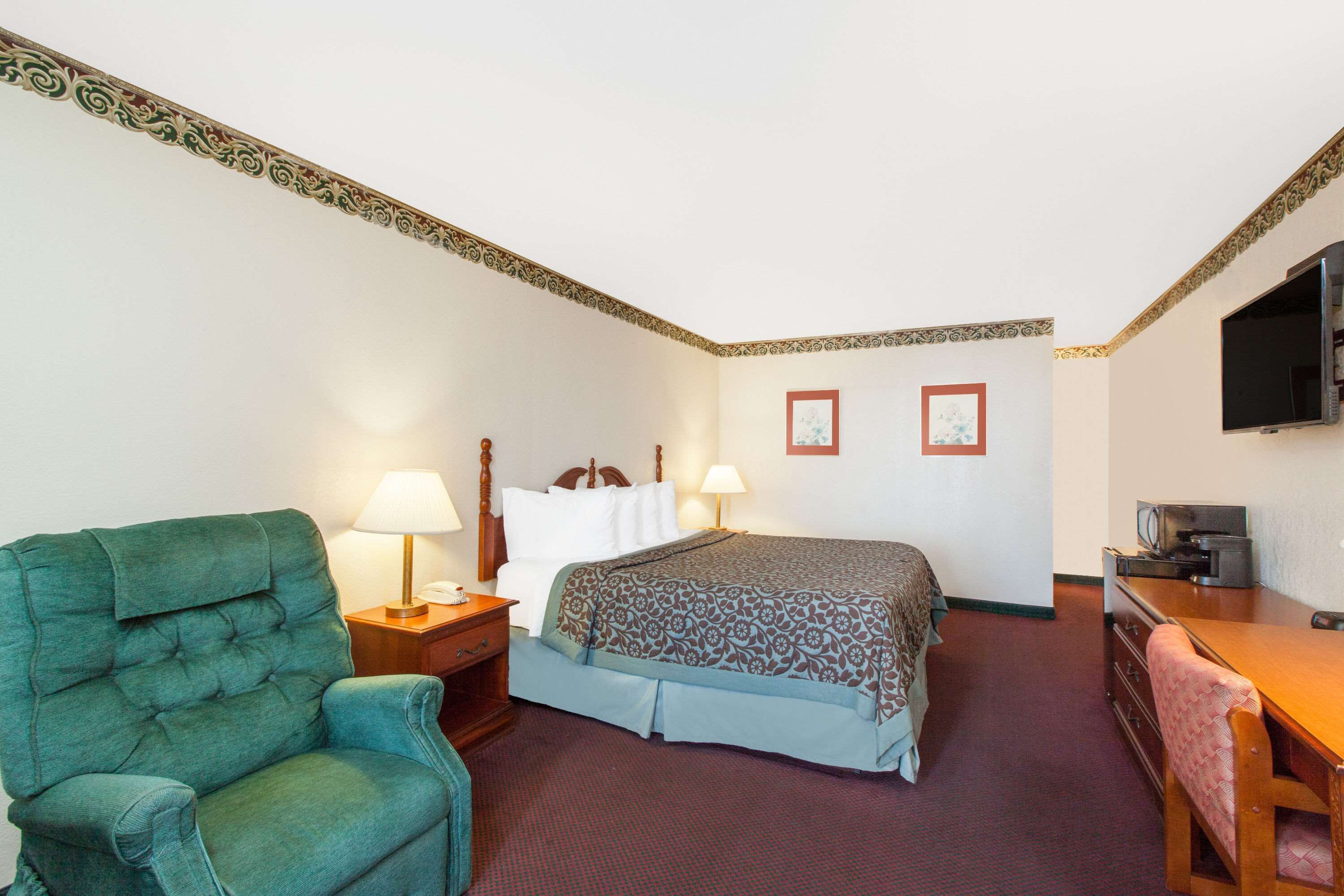A hotel room with a bed, a desk, a television, a chair, and two lamps.