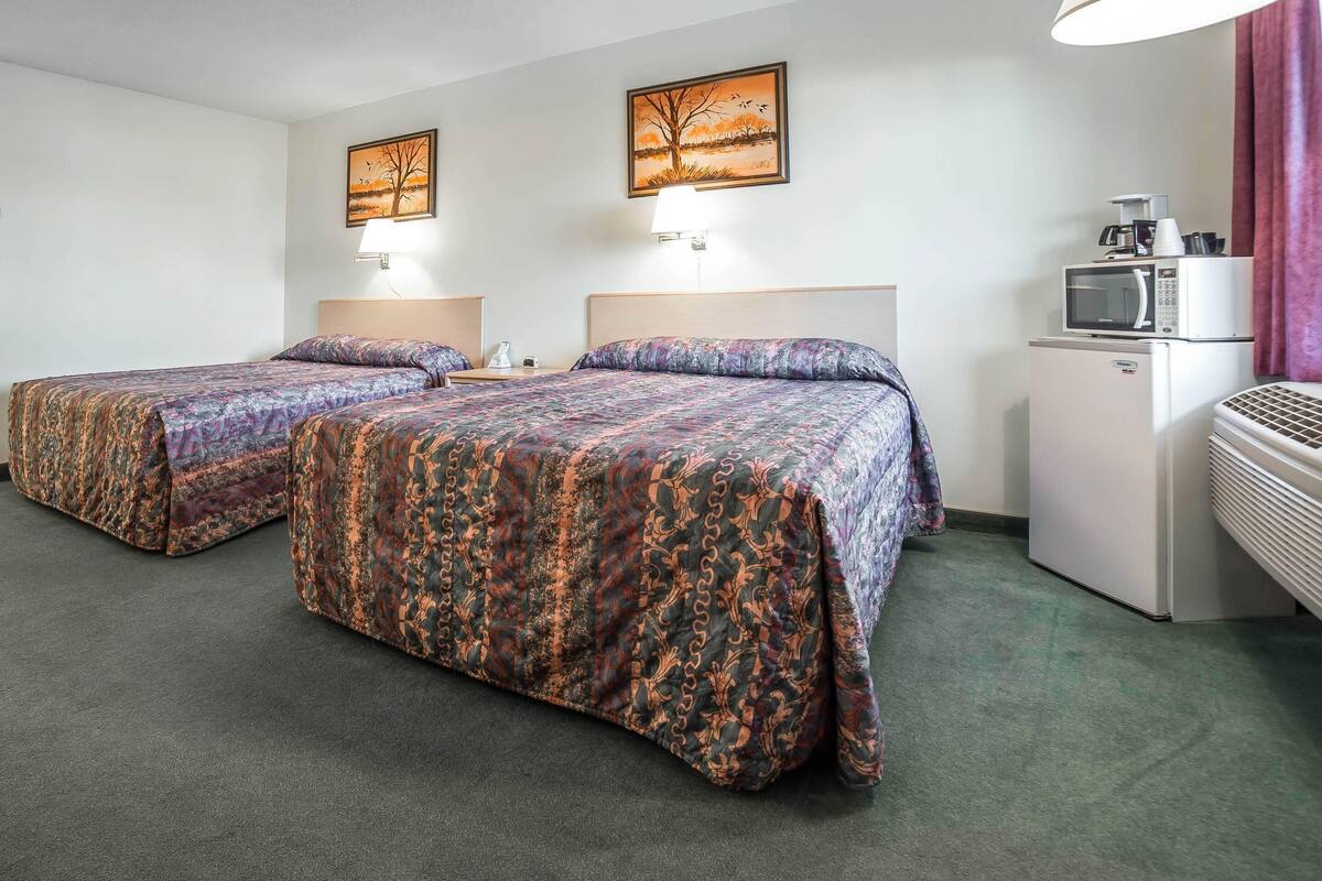 A hotel room with two beds, a microwave, a refrigerator, and a painting on the wall.