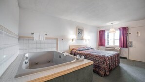 A room with a large bathtub, two beds with floral bedding, a window with curtains, and a wall-mounted picture. - Rodeway Inn Boardman - Hermiston (Boardman)