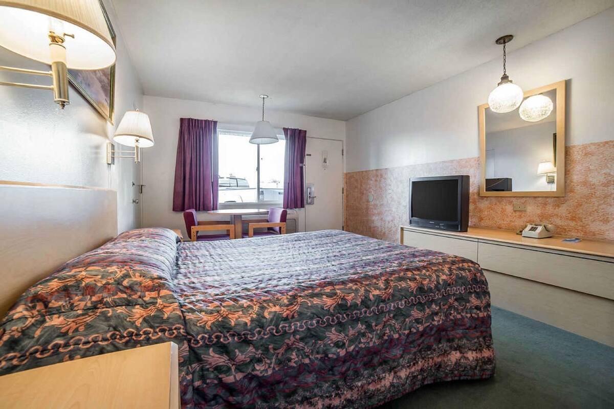 A hotel room with a bed, a desk, a television, and a window with curtains.