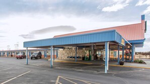 A motel with a covered parking area, a stone facade, and a red roof. - Rodeway Inn Boardman - Hermiston (Boardman)