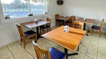 A dining area with wooden tables and chairs, a window with a view of trees, and a small plant on the wall.