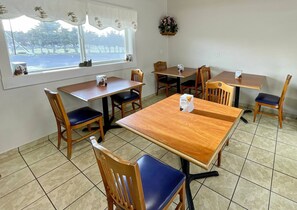 A dining area with wooden tables and chairs, a window with a view of trees, and a small plant on the wall.