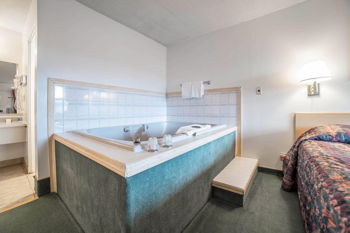 A room with a bathtub, a bed, a small table, and a wall-mounted light fixture.