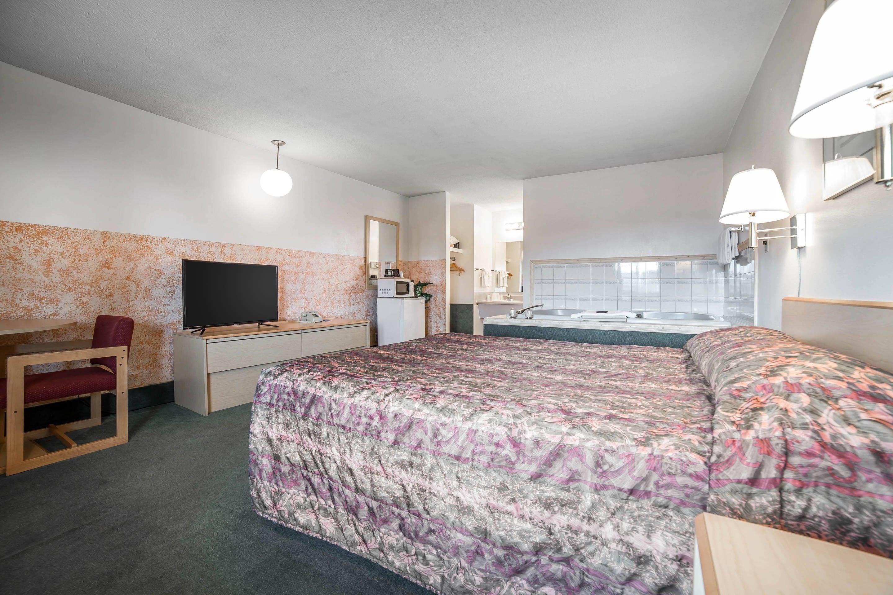 Hotellihuone, jossa on sänky, työpöytä, tuoli, televisio, pieni keittiö ja kylpyhuone.