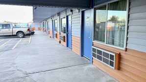 A row of motel rooms with blue doors and large windows, a covered parking area, and a beige pickup truck parked outside. - Rodeway Inn Boardman - Hermiston (Boardman)