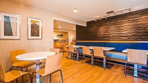Een modern restaurant met houten vloeren, ronde tafels en stoelen. Er hangen kunstwerken in lijsten aan de muren en de wand heeft een structuur.