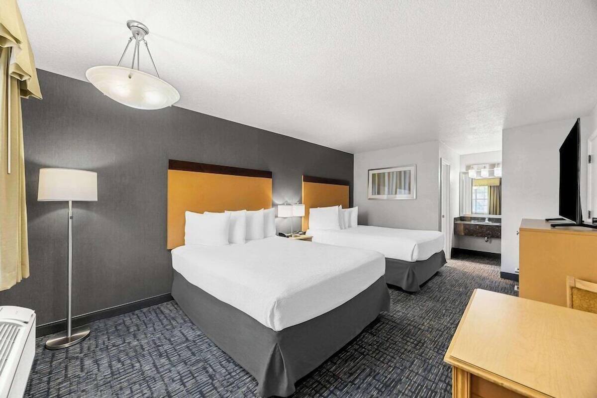 A hotel room with two beds, a desk, a TV, and a bathroom visible in the background.
