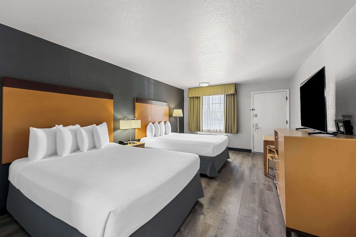 A hotel room with two beds, a desk, a television, and a window with curtains.