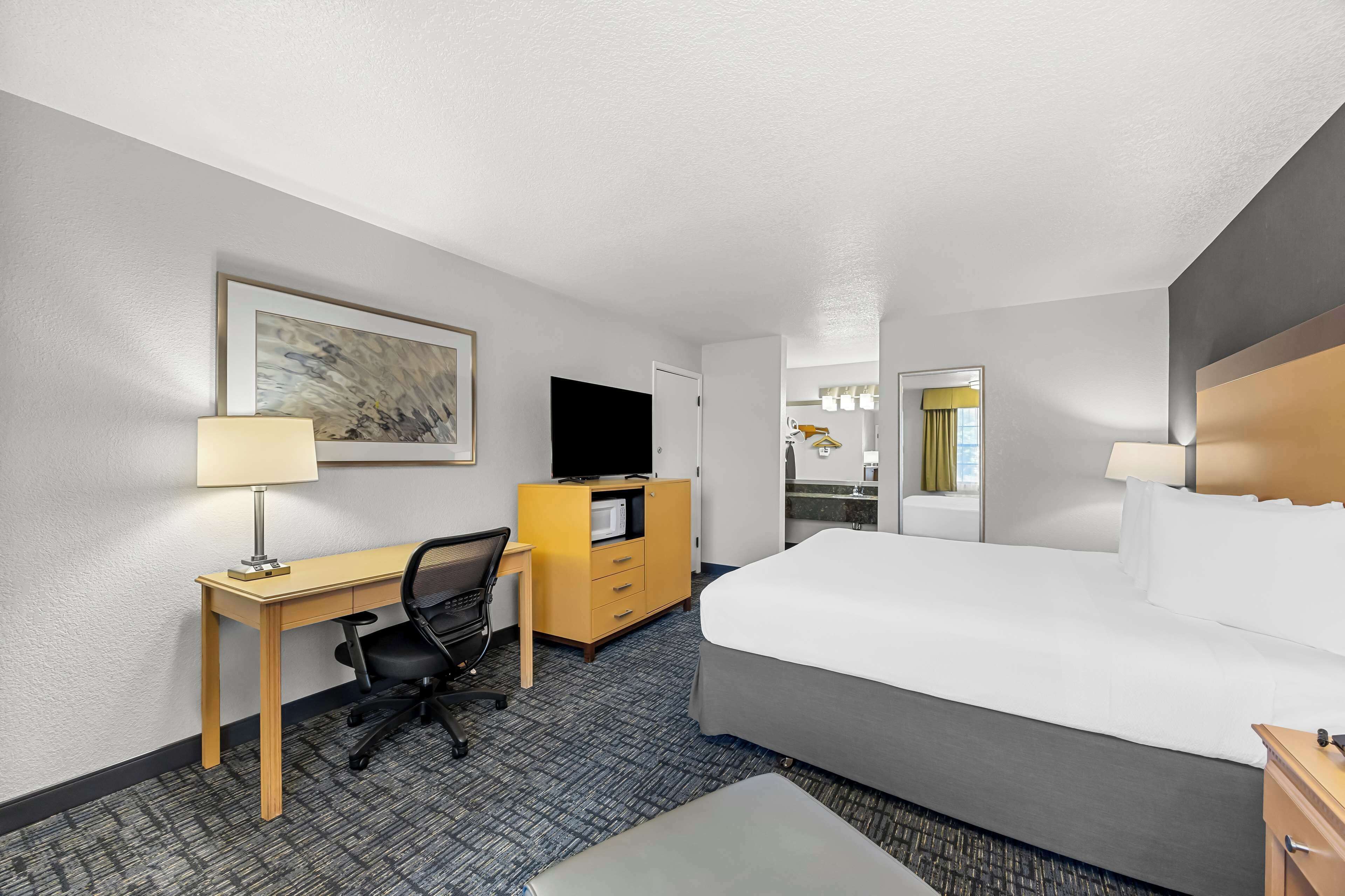 A hotel room with a bed, desk, chair, TV, and a dresser.