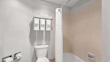 A bathroom with a toilet, a towel rack with folded towels, a shower curtain, and a small shelf with toiletries.