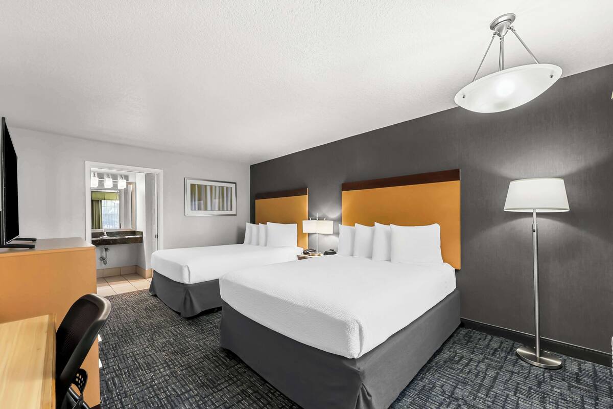 A hotel room with two beds, a desk, a chair, a desk lamp, and a TV.