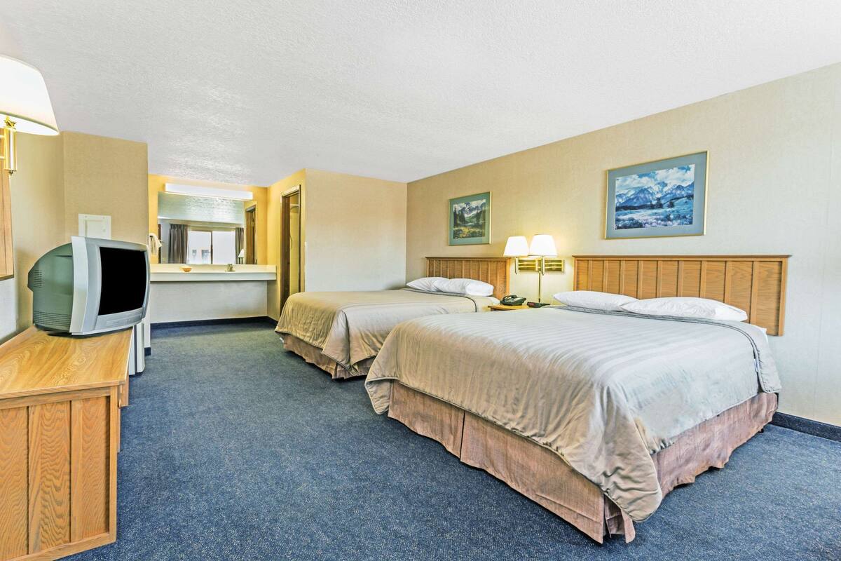 Une chambre d’hôtel avec deux lits, un bureau avec une télévision et une salle de bain visible au fond.