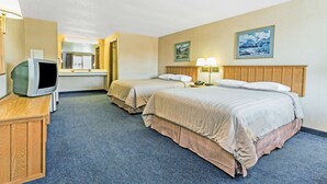 A hotel room with two beds, a desk with a television, and a bathroom visible in the background.