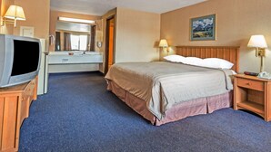 A hotel room with a bed, a television, a desk with a lamp, a mirror, and a painting on the wall. - Travelodge by Wyndham Pioneer Villa (Halsey)