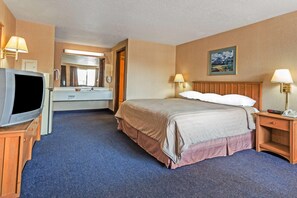 Habitación de hotel con una cama, televisión, escritorio, lámpara y un cuadro en la pared.