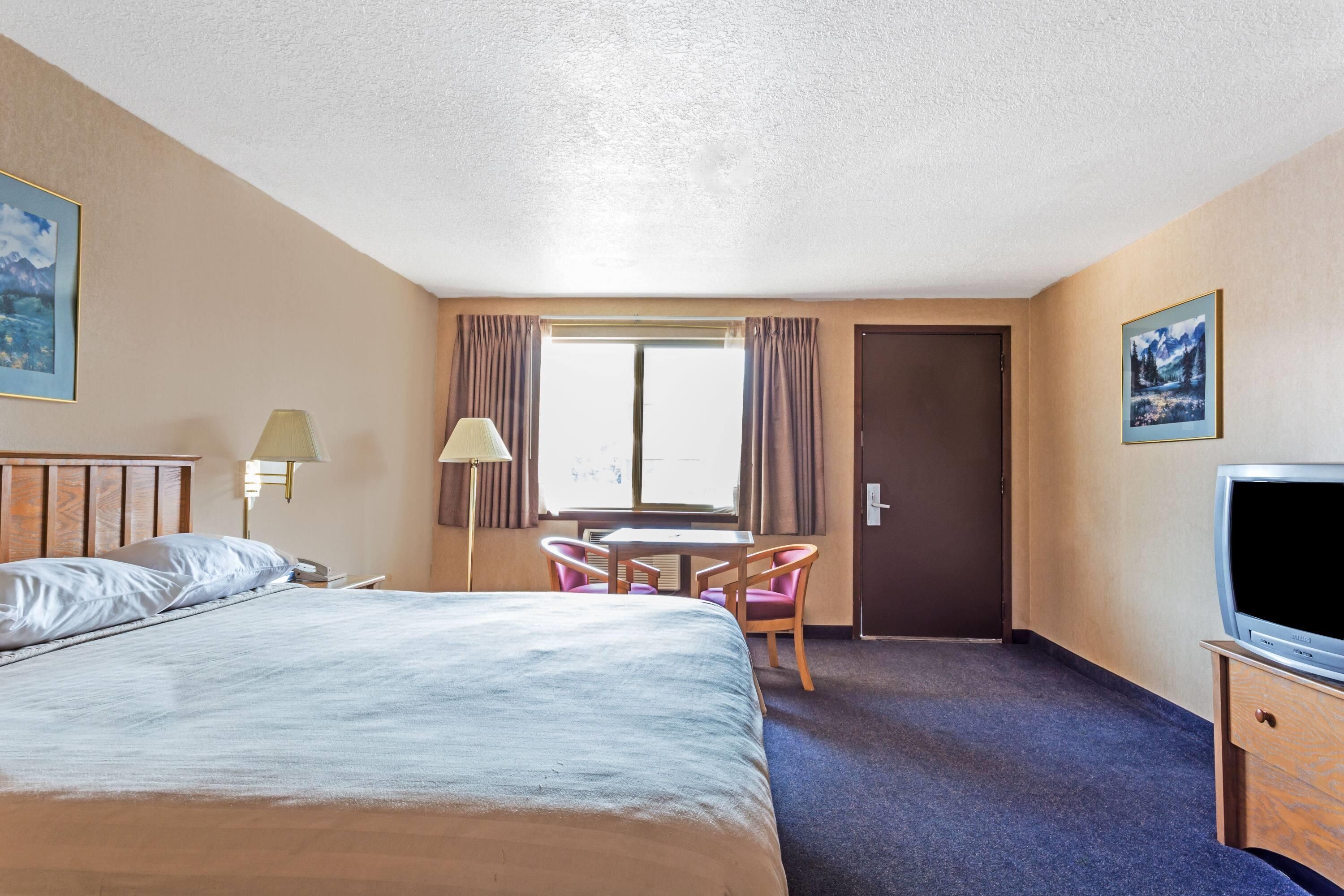 Una habitación de hotel con cama, escritorio, silla, televisor y puerta.