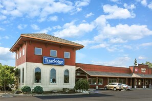 Un hotel Travelodge con fachada roja y color beige, un letrero llamativo y un estacionamiento con coches.