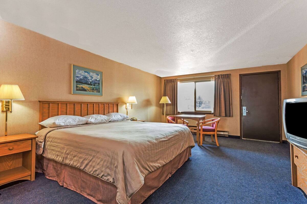 Une chambre d’hôtel comprenant un lit, deux lampes de chevet, un bureau avec une chaise, une télévision et une fenêtre avec des rideaux.
