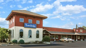 A Travelodge hotel with a red and beige facade, a signboard, and a parking lot with cars.