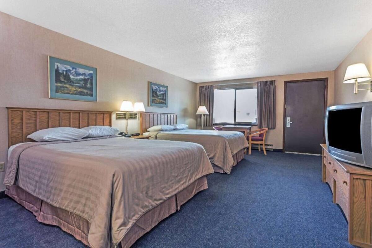 Une chambre d’hôtel avec deux lits, un bureau, une chaise, une télévision et deux tableaux au mur.