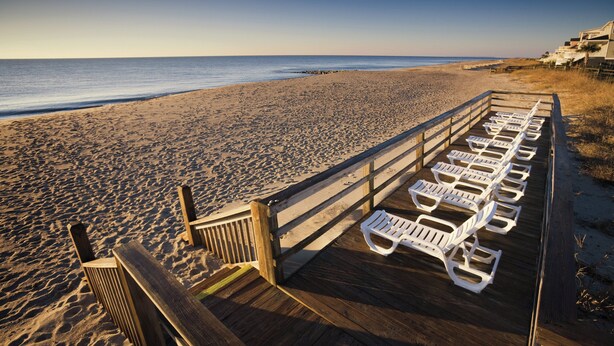 A wooden deck with white lounge chairs facing the beach. - Club Wyndham Ocean Ridge (Edisto Island)