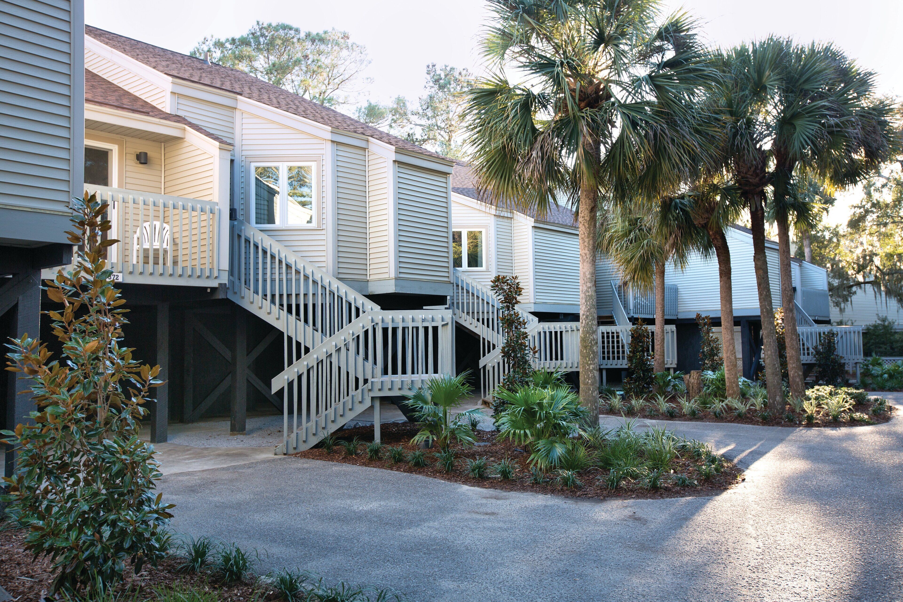 A row of two-story townhouses with a central staircase, surrounded by palm trees and a landscaped garden.