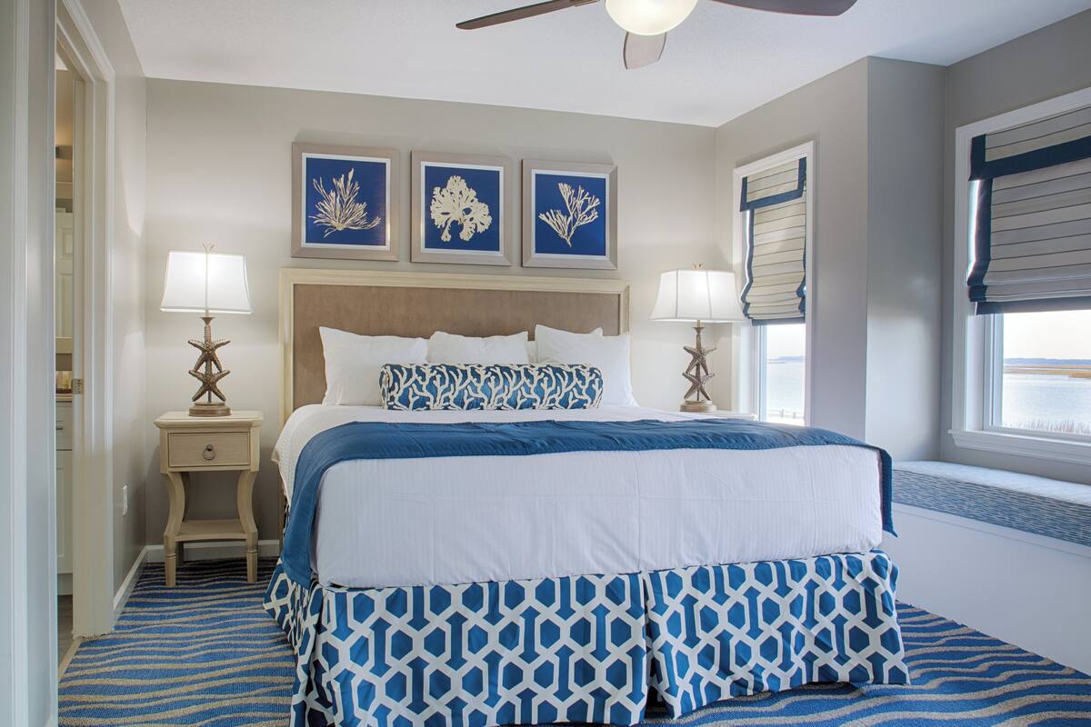 A bedroom with a bed, two bedside tables, a ceiling fan, and three framed wall art pieces.