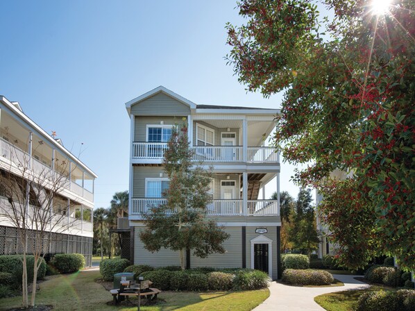 A multi-story residential building with a covered front porch, a small front yard with a picnic table, and a clear sky. - Club Wyndham Ocean Ridge (Edisto Island)