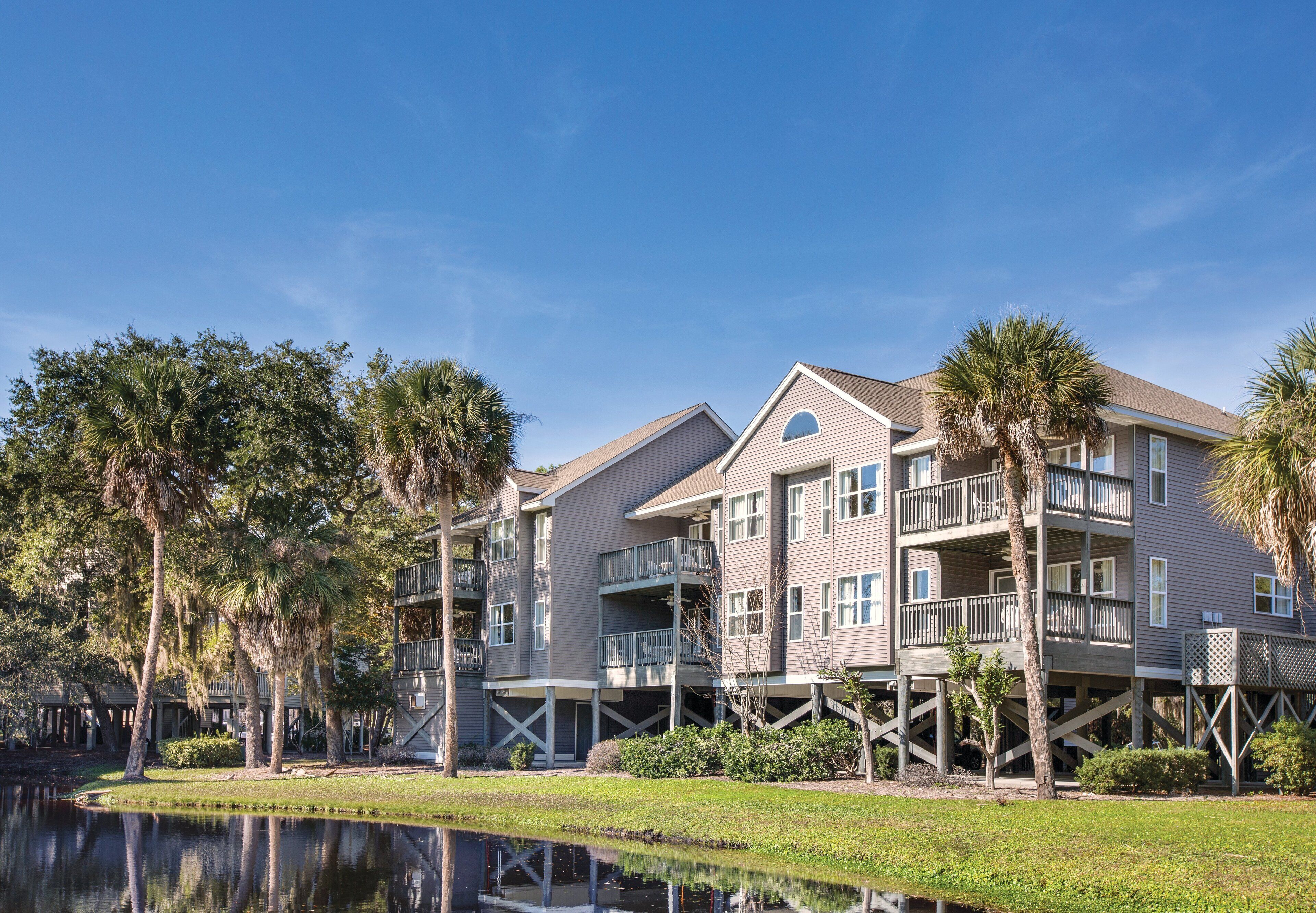 A multi-story building with balconies, a pond in the foreground, and palm trees.