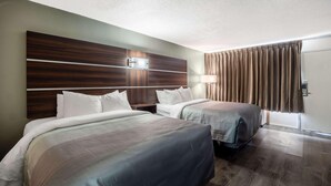 A hotel room with two beds, a wooden headboard, a nightstand, a lamp, and a window with curtains. - Motel 6 Yemassee, SC (Yemassee)