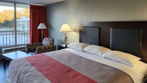 A hotel room with a large bed, a chair, a table, and a lamp. - Motel 6 Yemassee, SC (Yemassee)