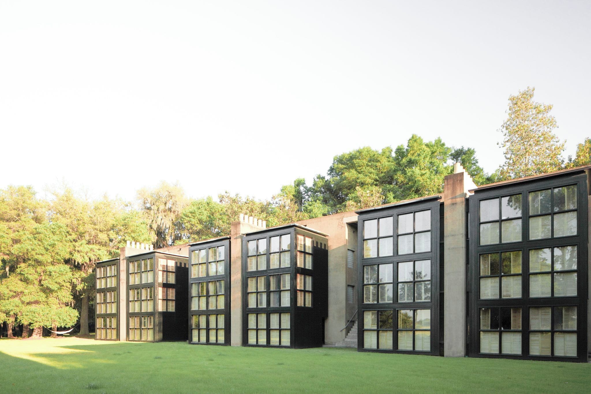 Un edificio moderno con ventanas amplias y techo plano, rodeado de un césped cuidado y árboles.