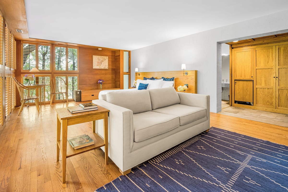 A modern living room with a sofa, wooden flooring, a blue patterned rug, and a wooden cabinet.