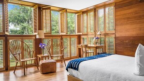 Un dormitorio con una cama grande, paredes de madera y varias ventanas con persianas.