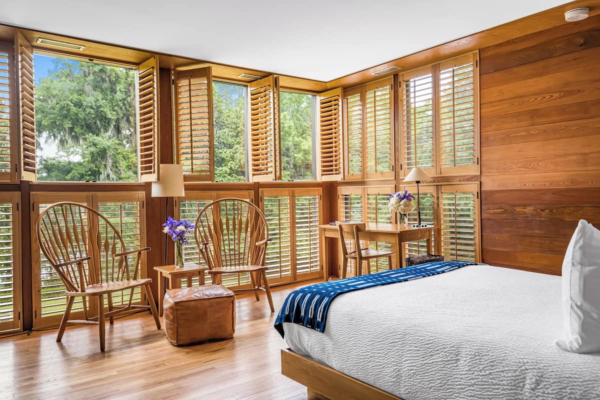 A bedroom with a large bed, wooden walls, and multiple windows with blinds.