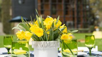 A dining table set with yellow flowers, green glassware, and a white vase.