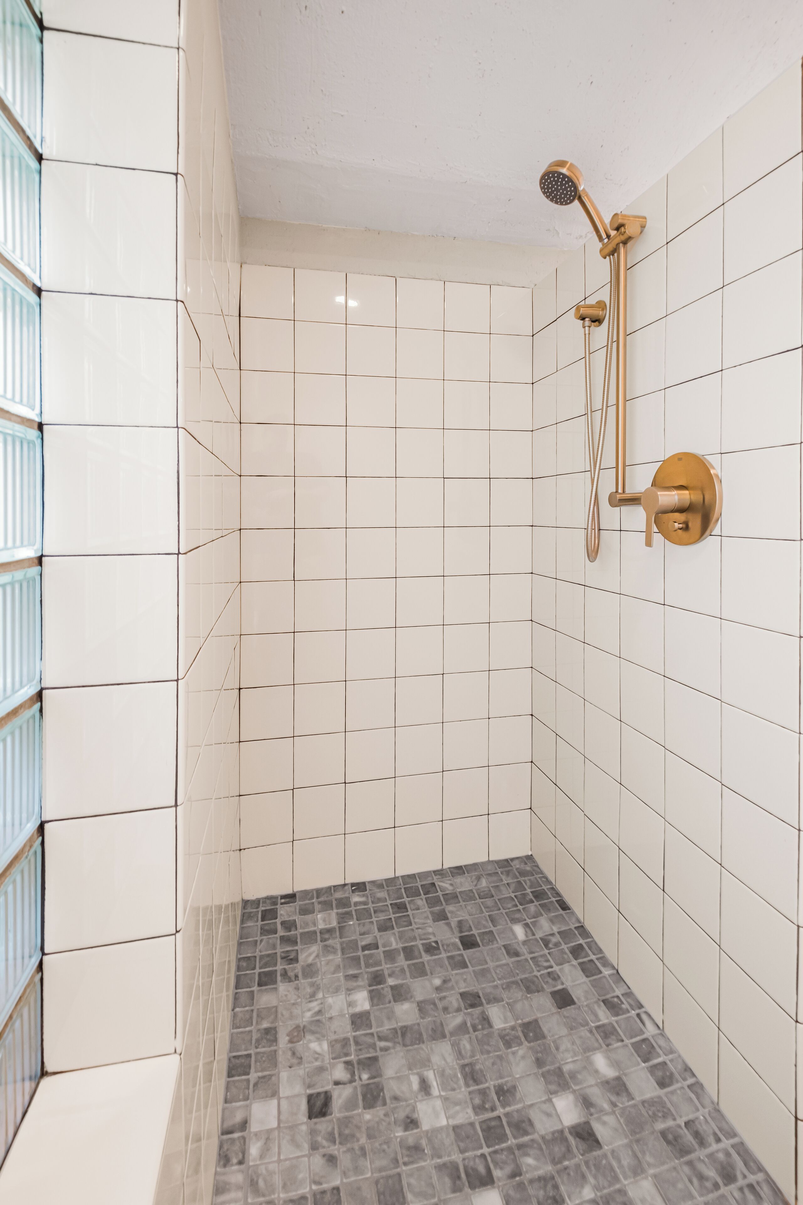 Un espace douche avec des murs recouverts de carreaux blancs et un sol carrelé.
