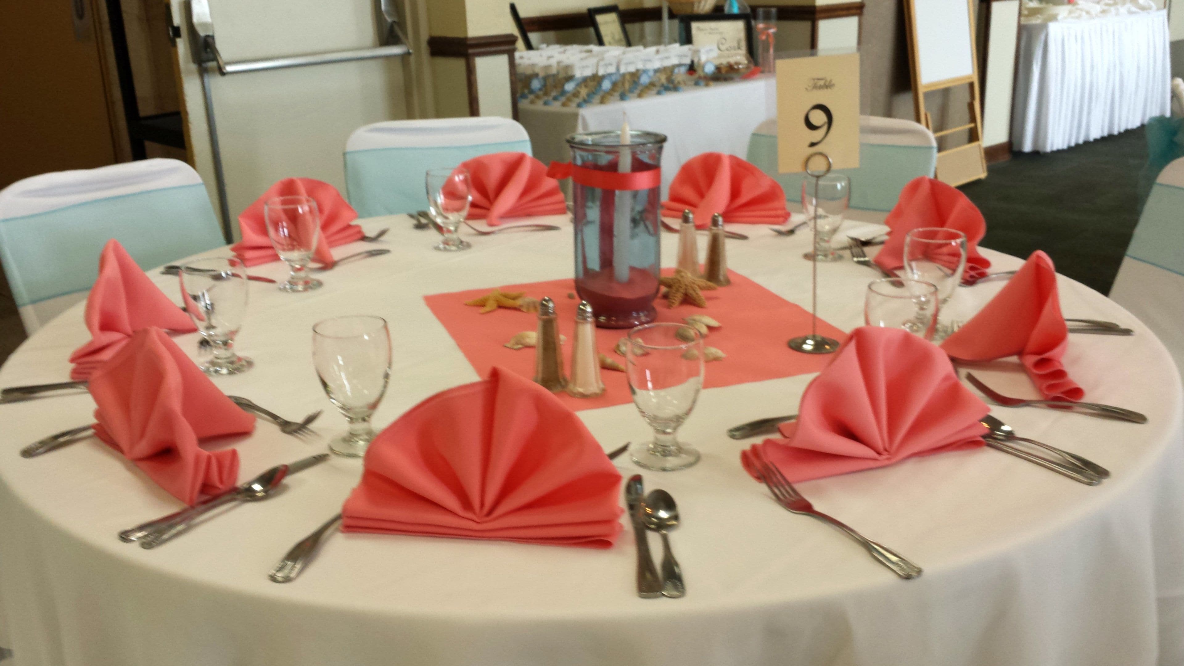 A round table set for a formal event with red napkins, clear glassware, and silverware.