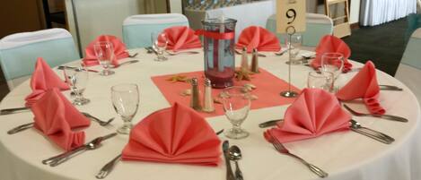 A round table set for a formal event with red napkins, clear glassware, and silverware.
