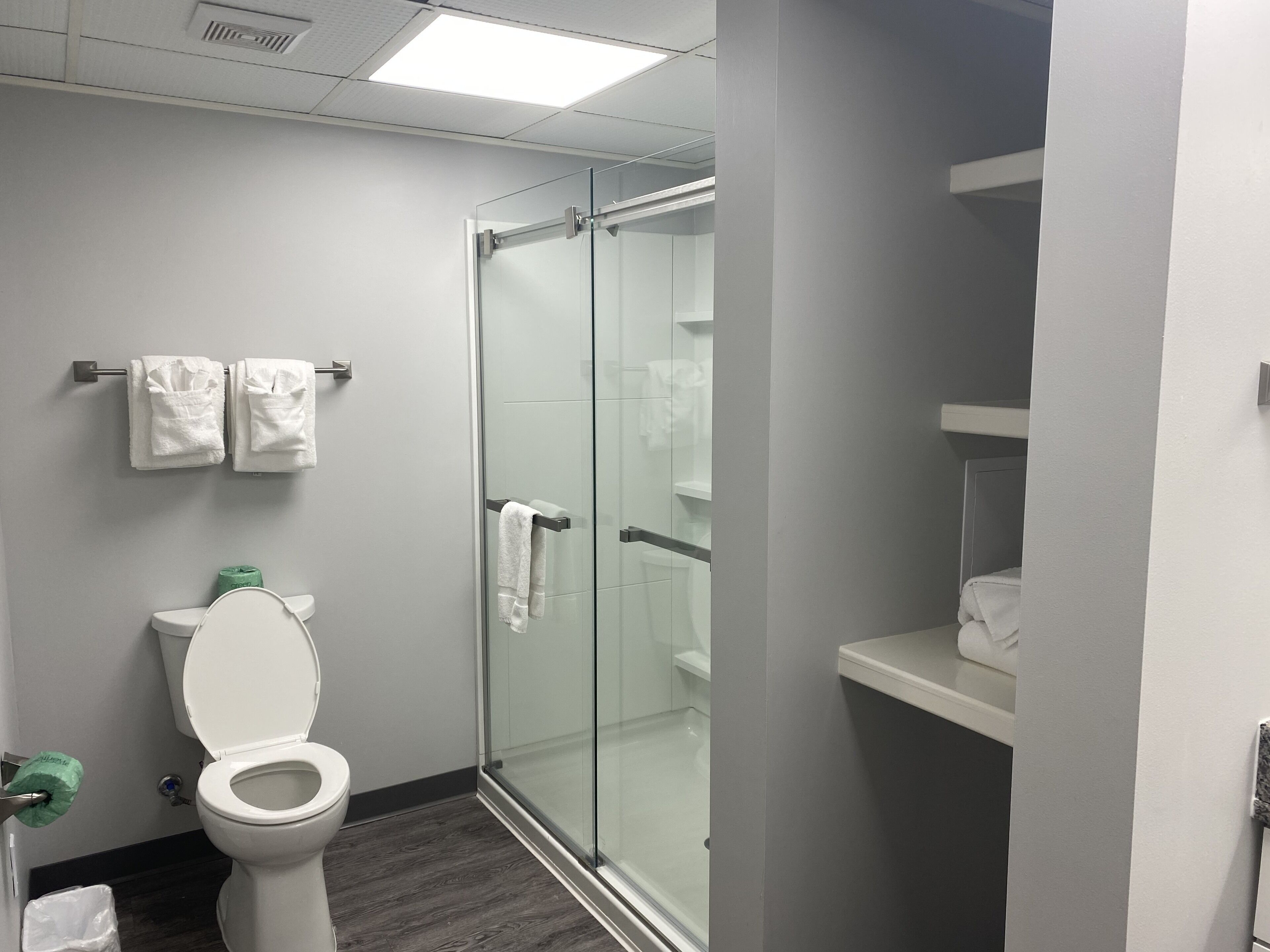 Un baño moderno con inodoro, cabina de ducha de vidrio y toallero con dos toallas.