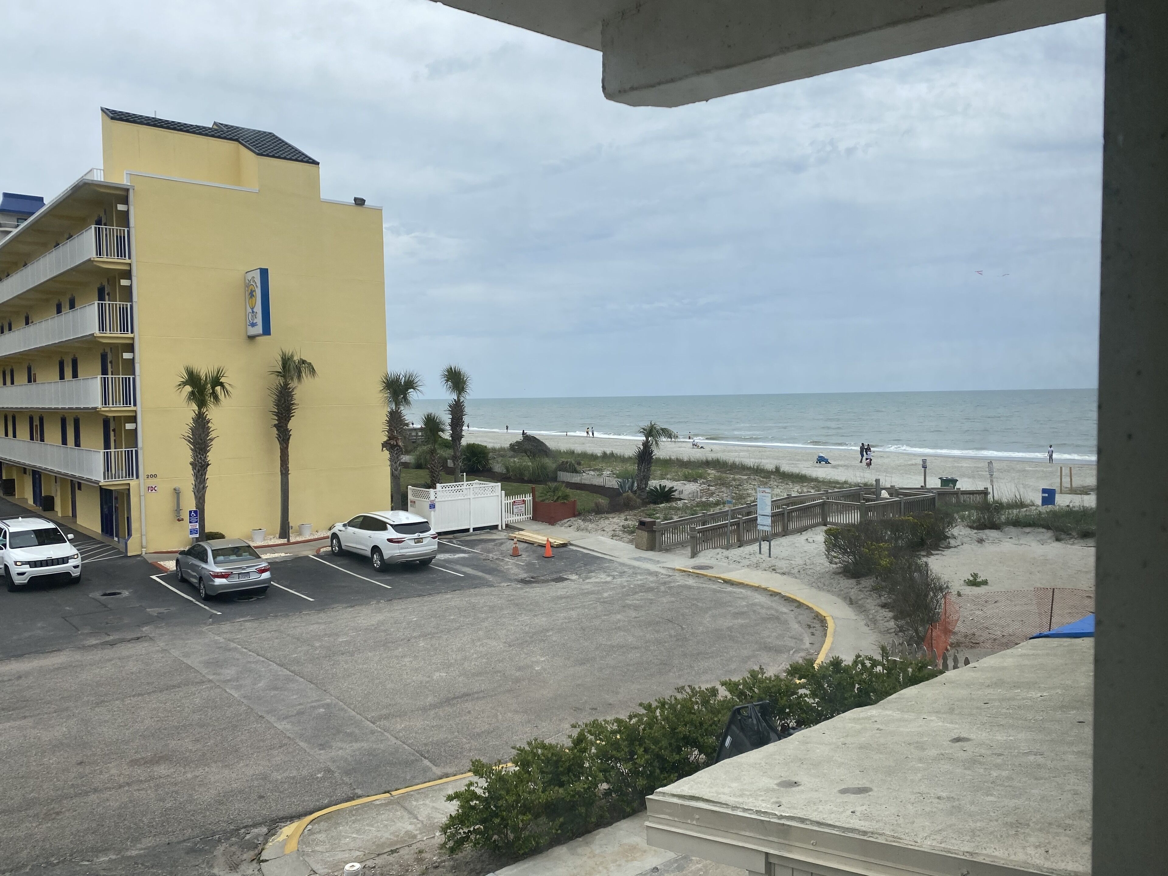 Un hotel con facciata gialla, un parcheggio e vista sulla spiaggia.