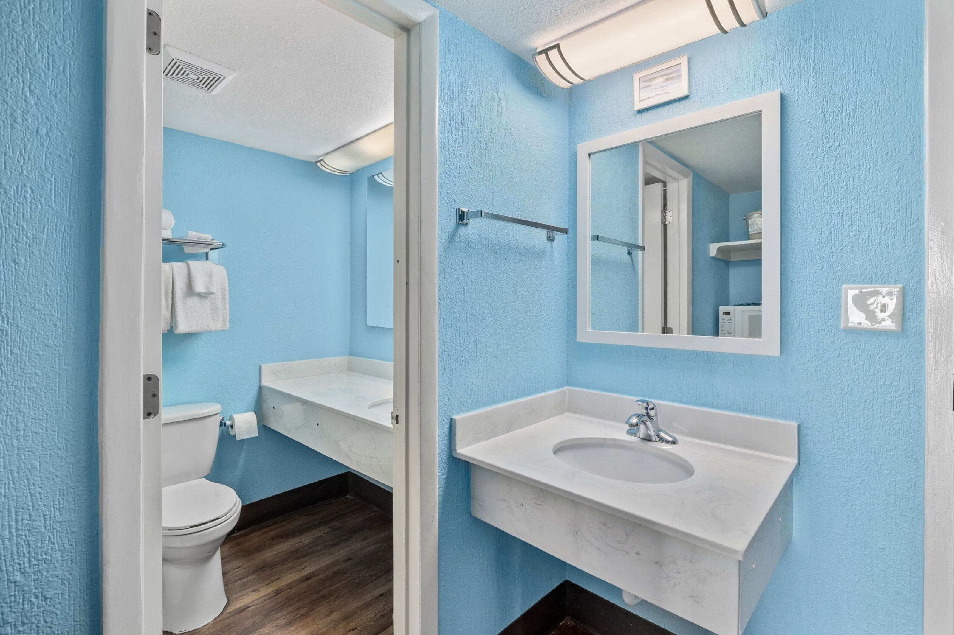 Ein Badezimmer mit blauer Wand, weißen Sanitärobjekten, einem Spiegel und einem Handtuchhalter.