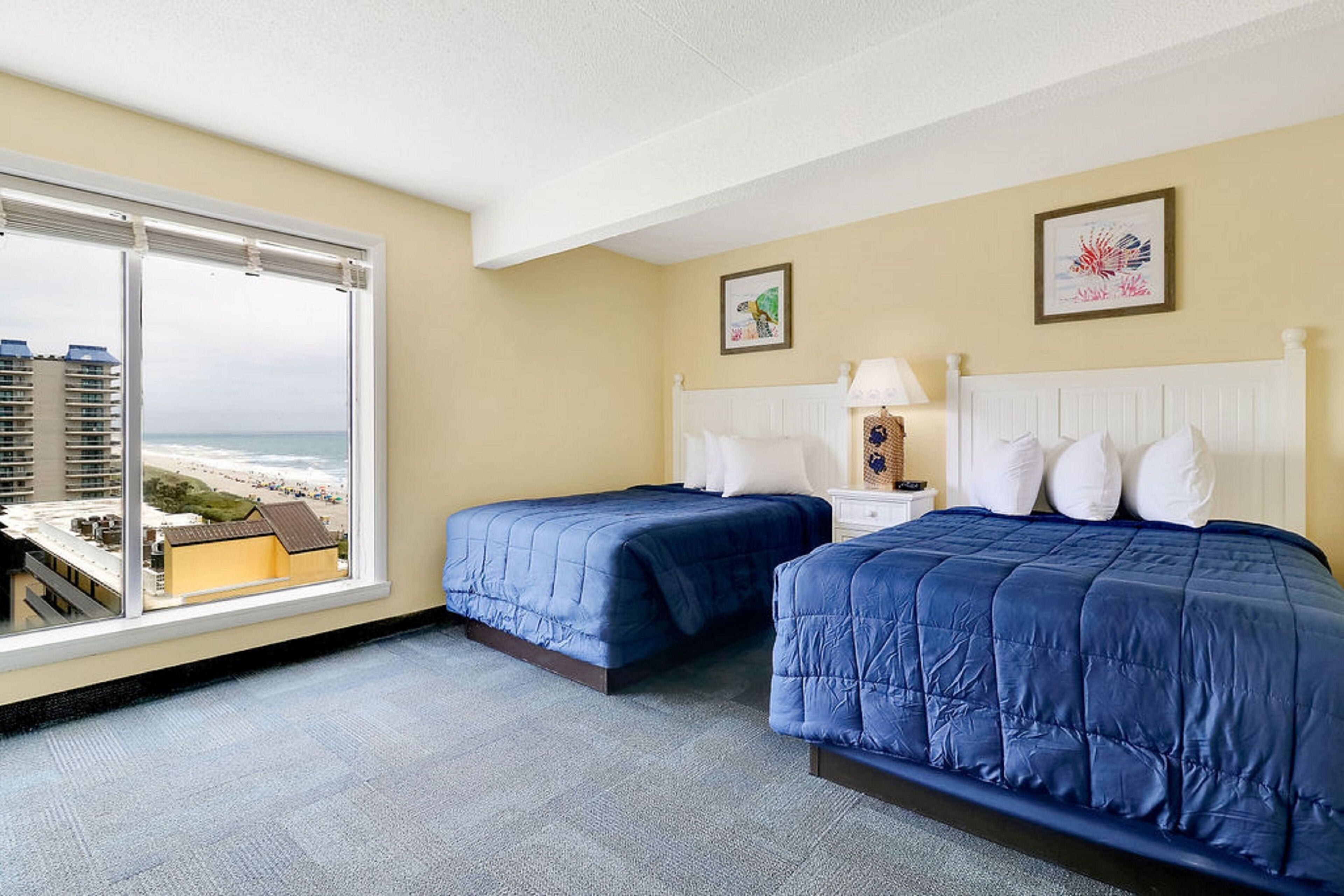 Une chambre d’hôtel avec deux lits, une grande fenêtre donnant sur la plage et des œuvres d’art accrochées aux murs.