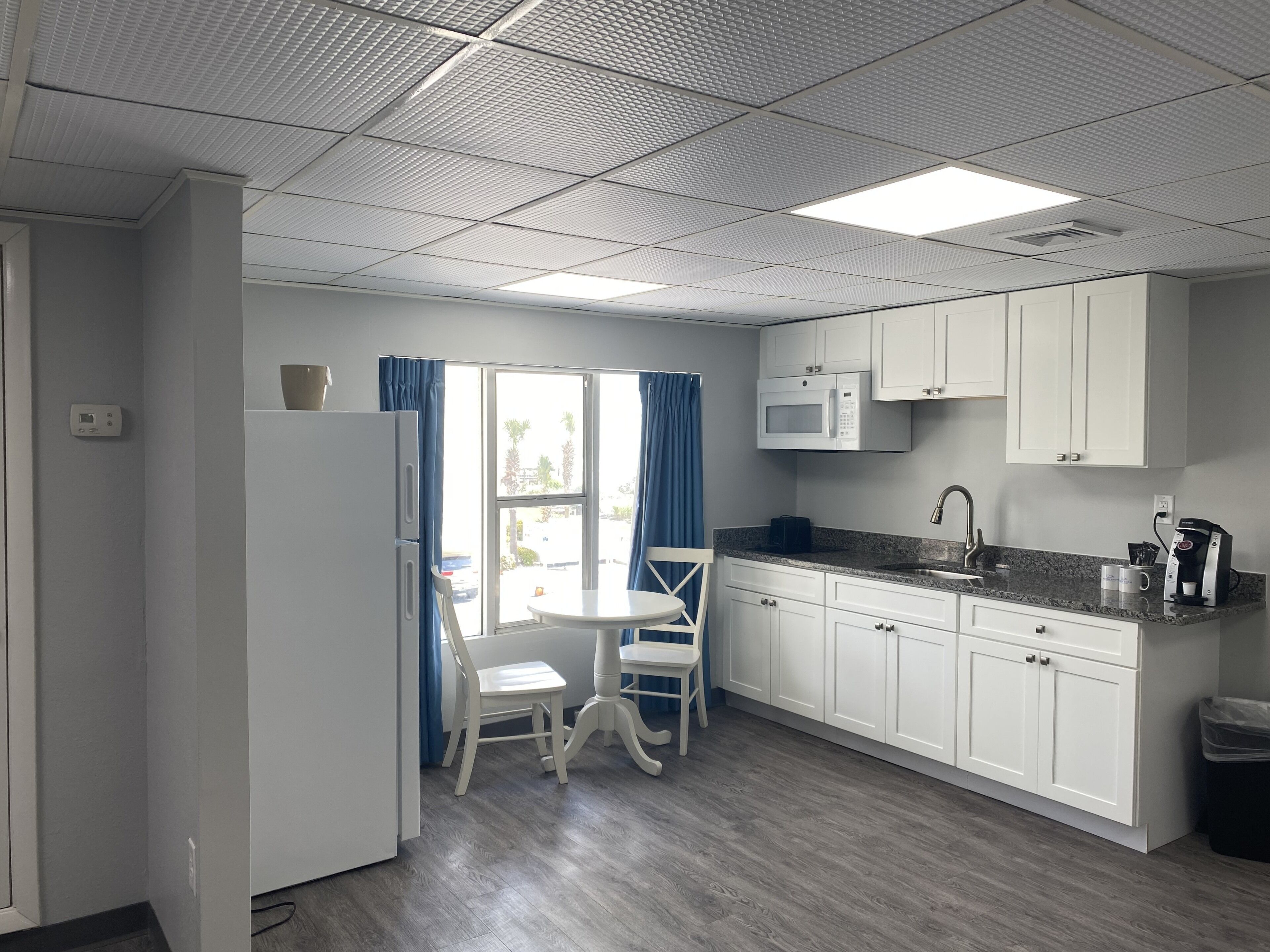 A compact kitchen with white cabinets, a microwave, a sink, and a coffee maker.