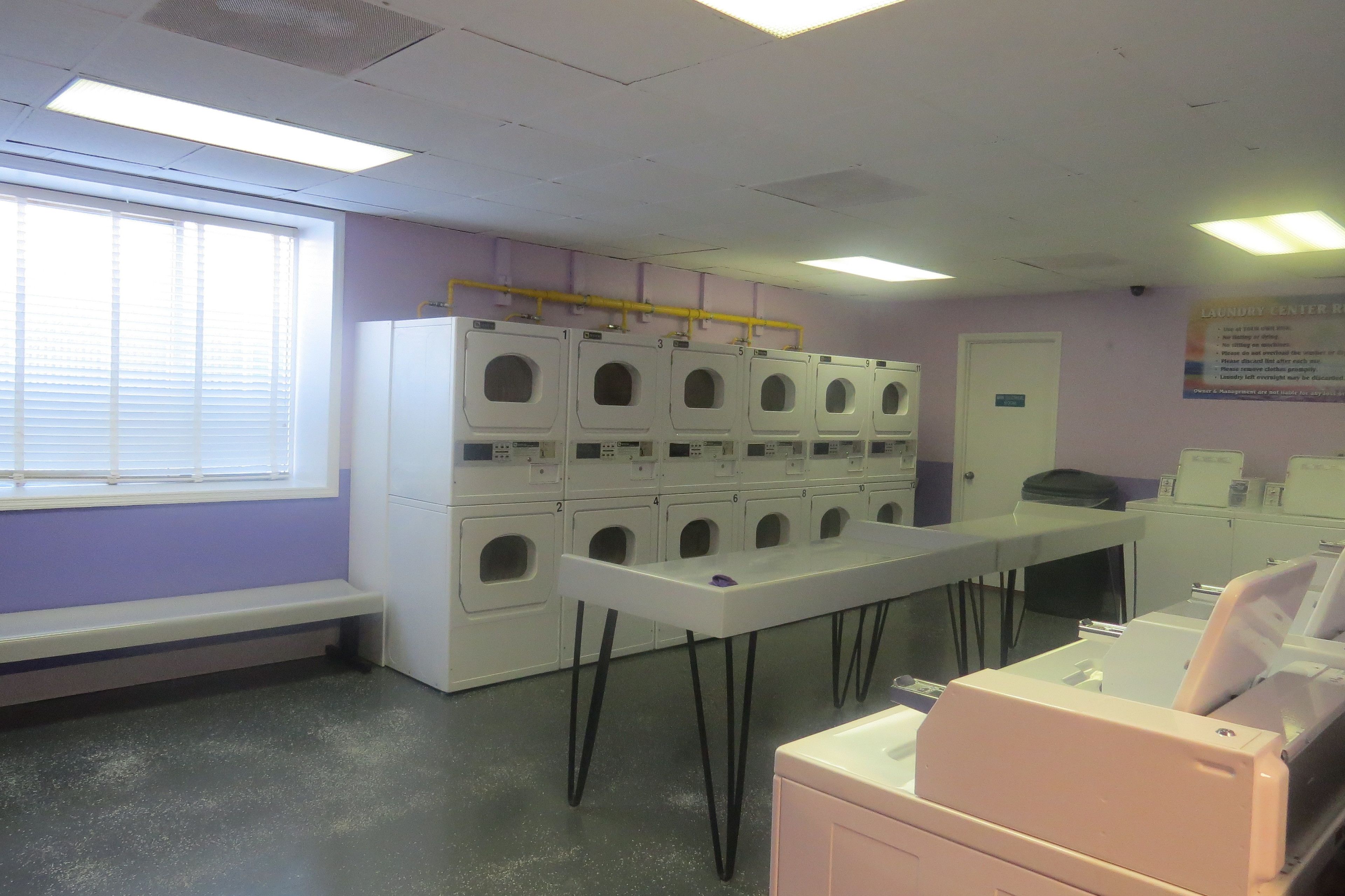 Une buanderie équipée de plusieurs machines à laver et de plusieurs sèche-linge, ainsi que d’un banc et d’une table.