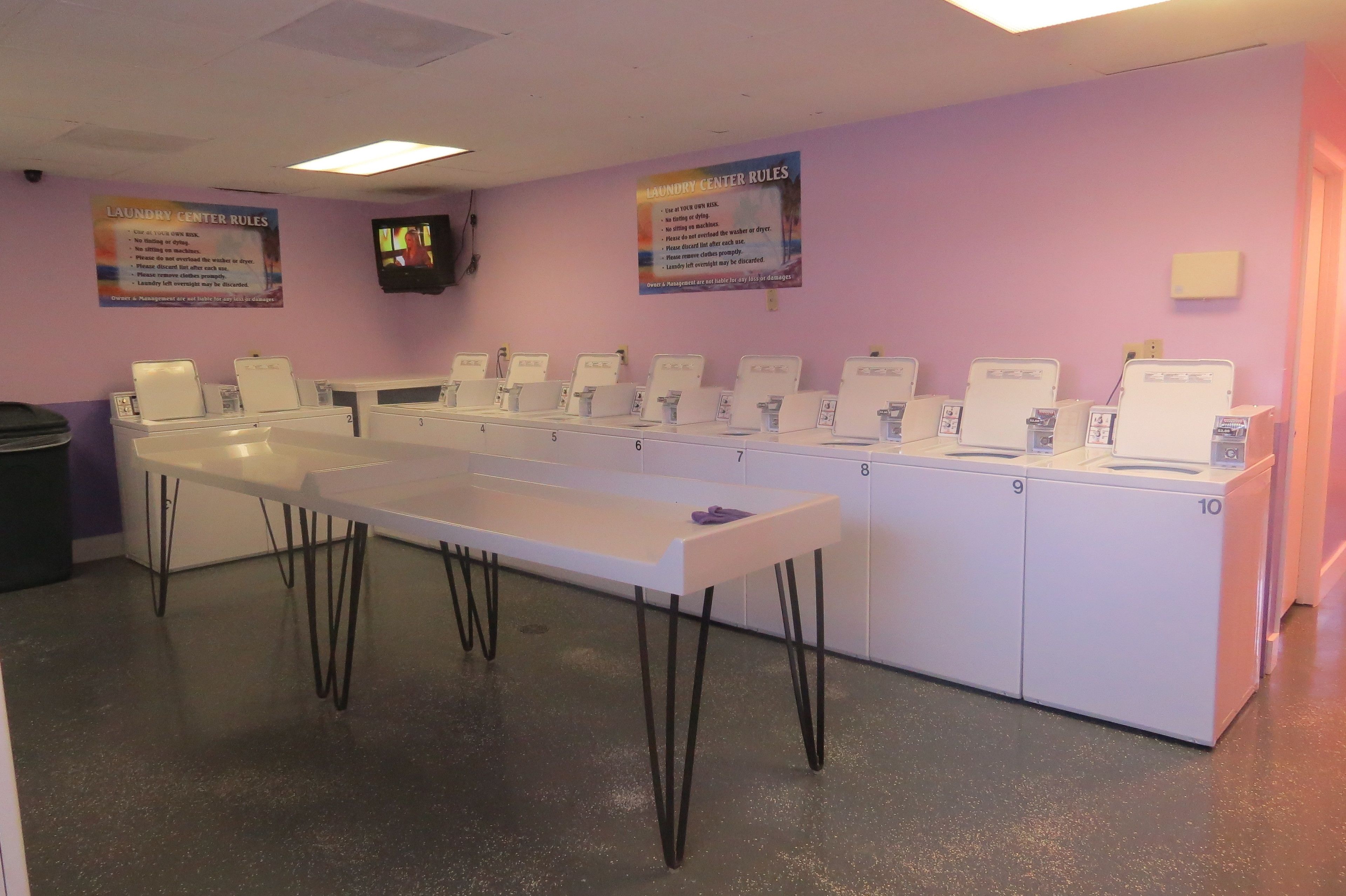 A laundry center with multiple washing machines and dryers, a table, and two signs with laundry center rules.